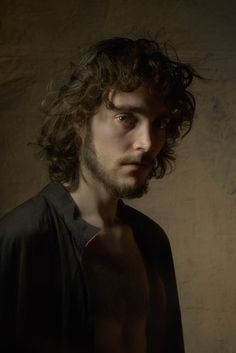 a man with long curly hair standing in front of a wall