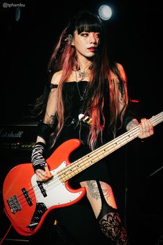 a woman with long hair and piercings holding a red bass guitar in her hands