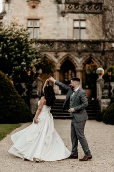 a bride and groom dancing in front of an old castle like building at their wedding