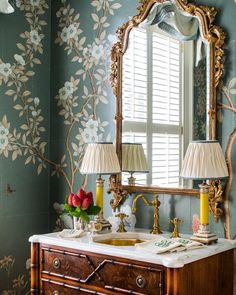 a bathroom vanity with a mirror, lamp and flowers on the wall next to it