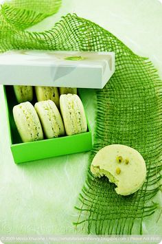 a box filled with green macaroons sitting on top of a white table cloth