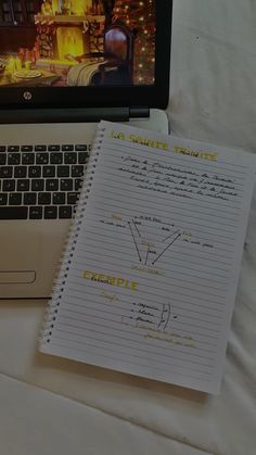 an open laptop computer sitting on top of a bed next to a notepad and notebook