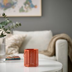 an orange vase sitting on top of a table next to a white couch and coffee table