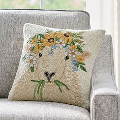 a white pillow with flowers on it is sitting on a gray chair in front of a window