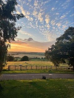 the sun is setting over an open field with trees and fence in the foreground