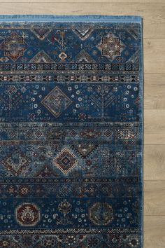 a blue rug with many different designs on the top and bottom, in front of a wooden floor