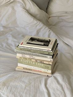 a stack of books sitting on top of a bed next to a white comforter