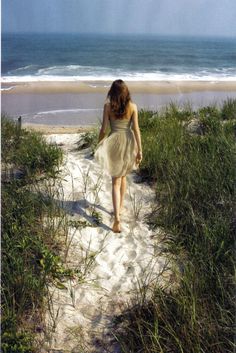 a woman walking down a path to the beach