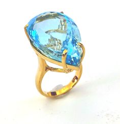 A stunning gold cocktail statement ring showcases a large pear cut 48.61 carats Natural Blue Topaz. A Premium Quality High End Blue Topaz  Gemstone.  The ring has been hand crafted in 10K Yellow Gold, but only UK hallmark it as 9K. It has been beautifully created with simple lines combine with big bold gemstone, a classic design with contemporary looks. Limited Edition. Clarity -Transparent Colour - Sparkling Blue Type - Natural Topaz 9K Yellow Gold with UK HALLMARKED Individually Hallmarked to British standards at the London Assay Office Blue Topaz Stone size:  26.8 mm Length * 17 mm Width * 14 mm Depth, 48.61 carats   Total ring size size : 27 mm Length * 17 mm Width * 14.5 mm Depth of stone sit on the finger Ring size: P  (UK), 7 ¾ (US) Ring band width : 3.7 mm approx... Ring band thick Green Emerald Ring, Gold Solitaire Ring, Blue Topaz Stone, Gold Cocktail, Etsy Gold Ring, Royal Jewels, Peridot Ring, Swiss Blue Topaz, Topaz Stone