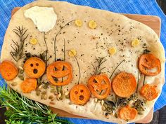 a pizza topped with sliced up carrots on top of a wooden cutting board next to herbs