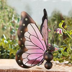 a pink and black butterfly sitting on top of a piece of wood next to flowers