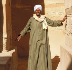 a man standing in front of a stone pillar with his hands out and wearing a turban