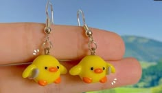 a pair of yellow rubber ducky earrings with dangling hooks in front of a mountain scene