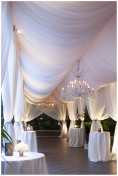 an indoor wedding venue with white draping and chandeliers