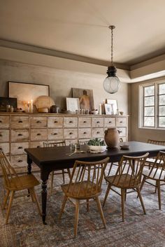 a dining room table surrounded by chairs in front of a dresser and window with candles on it