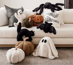 a white couch topped with lots of stuffed animals next to pumpkins and ghost pillows