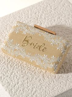 Meet your favorite summer clutch for the bride to be in your life, the Fiorentina "Bride" Minaudiere from Shiraleah. This clutch features a floral embroidery and the text "Bride" in gold cursive lettering and a wooden closure. This bag will go perfectly with any of the bride to be's outfits making it look chic and sophisticated. Measuring L 8" × W 2" × H 4.25"; and a 23" L cross body chain , the Fiorentina "Bride" Minaudiere effortlessly exudes style and sets a statement. Pair with other items f Elegant Summer Wedding Clutch, Summer Wedding Clutch Evening Bag, Gold Clutch For Formal Summer Events, Gold Embroidered Clutch For Wedding, Rectangular Gold Clutch For Summer, Gold Rectangular Clutch For Summer, Embroidered Clutch As Summer Gift, Gold Evening Bag For Summer Wedding, Embroidered Clutch For Summer Gift