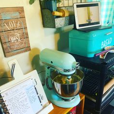 a blue mixer sitting on top of a wooden table next to a laptop and other items