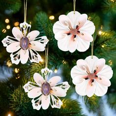 three ornaments hanging from a christmas tree decorated with pink and white paper flowers on them