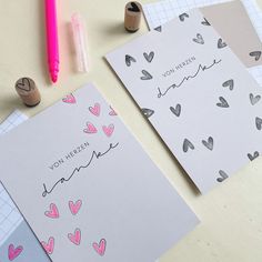 two greeting cards with hearts on them next to markers and pens