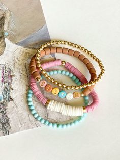 four bracelets with beads and charms on top of a piece of paper next to a photo