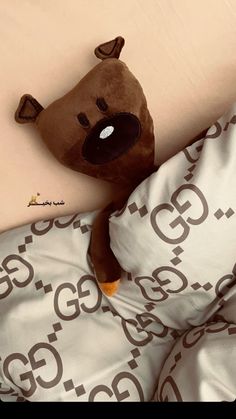 a brown teddy bear laying on top of a bed under a comforter and pillow