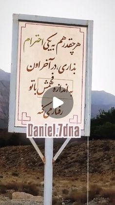 a sign in arabic on the side of a road with mountains in the back ground