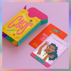 two cards are sitting next to each other on a pink surface with an orange and yellow box