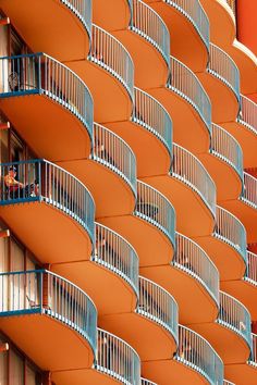 an orange building with balconies and people on the balconys looking out at the street