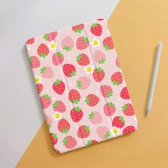 a pink notebook with strawberries on it next to a white pen and orange background