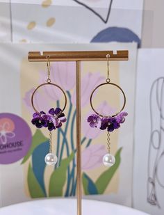 a pair of earrings with purple flowers and pearls hanging from the end of each ear