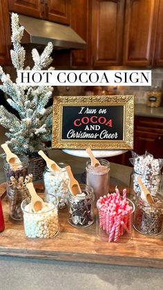 hot cocoa sign and christmas - cheer candy in jars on a kitchen counter with wooden spoons