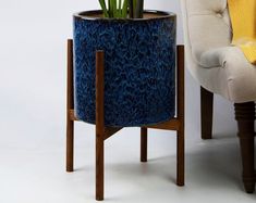 a blue planter sitting on top of a wooden stand next to a white chair