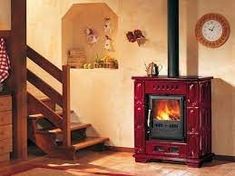 a red stove sitting inside of a living room next to a stair case and clock