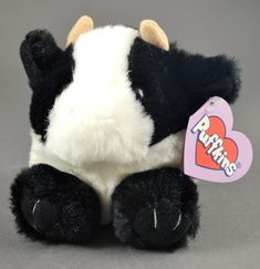 a black and white stuffed cow with a heart tag on it's ear, sitting against a gray background