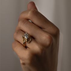 a woman's hand holding a ring with a diamond in it and gold band