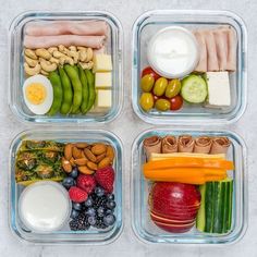 four plastic containers filled with different types of food and fruit, including eggs, cucumbers, tomatoes, grapes, cheese, and meats