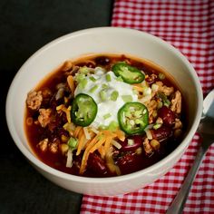 a white bowl filled with chili, cheese and other toppings on top of a checkered table cloth