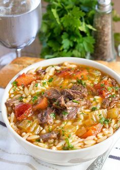 a white bowl filled with meat and rice soup next to some bread on a table