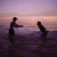 two people playing in the ocean at sunset