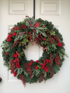 a wreath hanging on the front door of a house with red berries and greenery