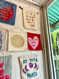 several colorful handmade wall hangings on the side of a building with words written on them