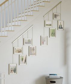 a white staircase with pictures on the wall and a trash can under it next to a stair case