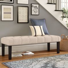 a beige bench sitting in front of a stair case with pictures on the wall behind it