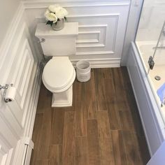 a white toilet sitting inside of a bathroom next to a bath tub and wooden floors