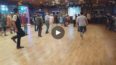 a group of people are dancing in a large room with wooden floors and ceiling lights