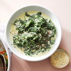 a white bowl filled with broccoli and cheese on top of a pink table