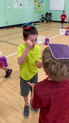 two young boys standing in a gym with one holding his hand up to his face