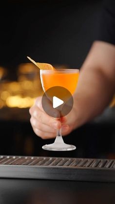 a person holding a cocktail glass with an orange garnish on it and the video below