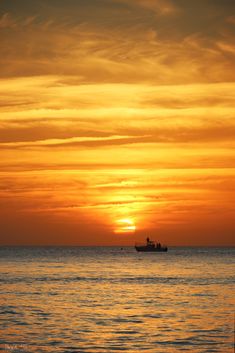 the sun is setting over the ocean with a boat in the distance